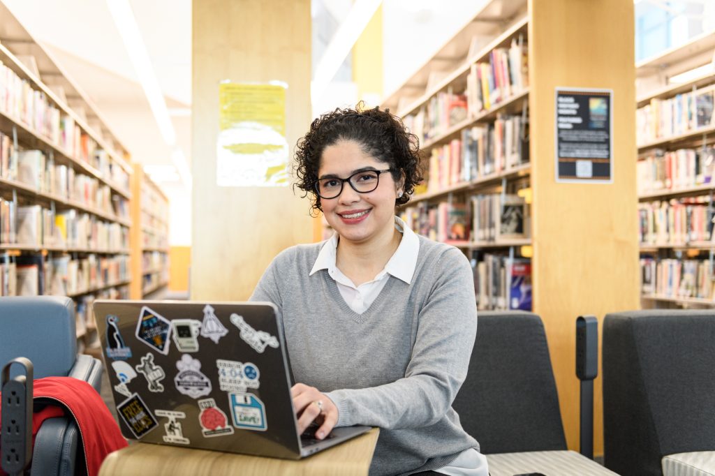 Young woman typing on laptop at desk, in a library.