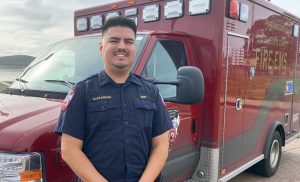 Alex Moya in EMS uniform standing in front of an EMS Firetruck