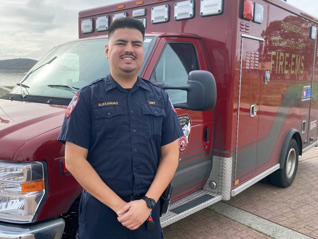 Alex Moya in EMS uniform standing in front of an EMS Firetruck