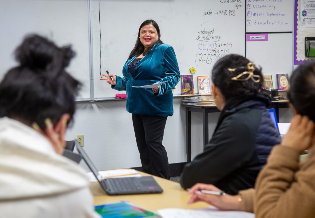 Shilpi Nandra, wearing a blue blouse, stands in front of a white board and teaches a class of students