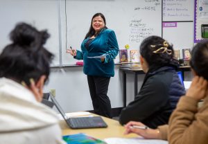Shilpi Nandra, wearing a blue blouse, stands in front of a white board and teaches a class of students