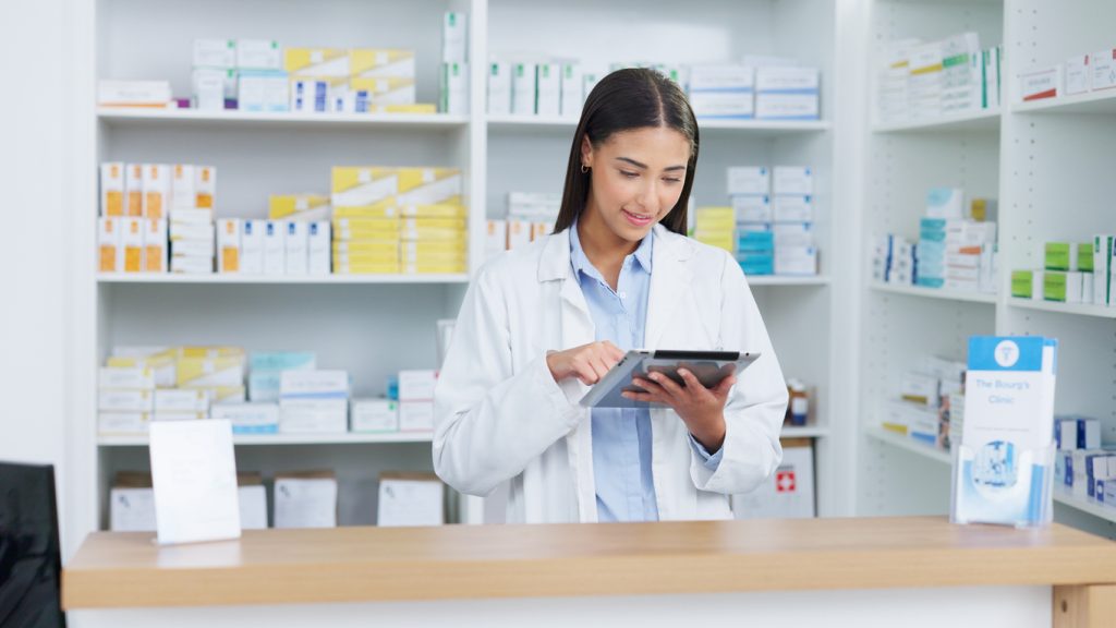 Portrait of a cheerful and friendly pharmacist using a digital tablet to check inventory or online orders in a chemist. Young latino woman using pharma app to do research on medication in a pharmacy