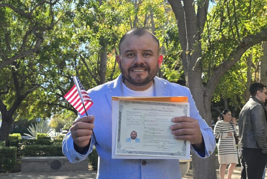 César Omar Cuenca Camacho holding his citizenship certificate and an American Flag
