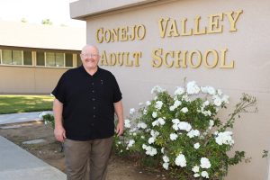 Mike Sanders standing in front of a Conejo Valley Adult School Sign