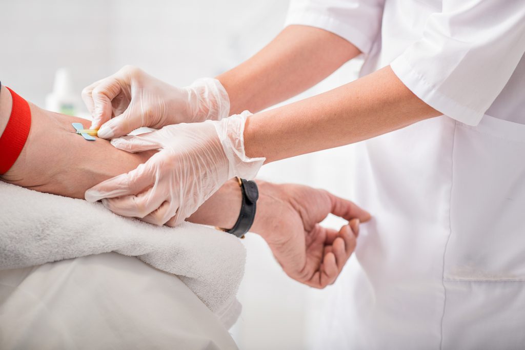 Close up of doctor arms sticking needle into male arm for blood sampling