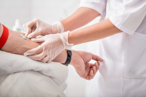 Close up of doctor arms sticking needle into male arm for blood sampling