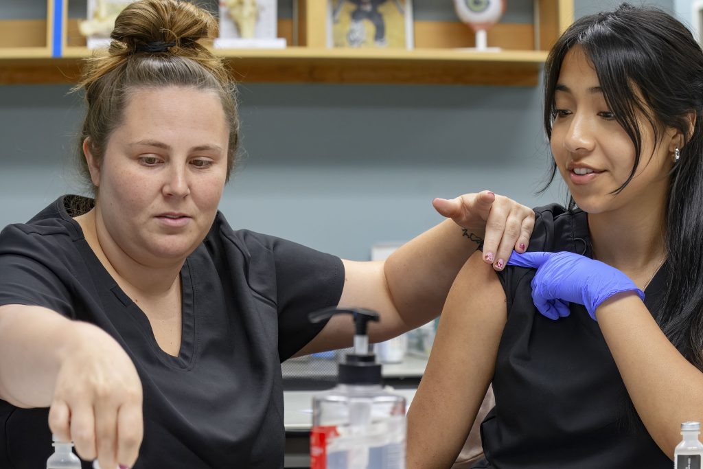 Amber Rosas practices giving a vaccination to fellow student Iveth Gonzalez during her medical assisting class at the Lompoc Adult School and Career Center (LASCC). She returned to school after becoming a single mother of two and needed a career to support her family. She says Lompoc’s program’s affordable cost and the support she received from teachers and staff were vital to her success. She received a medical certification and now works as a social service assistant at a nursing/rehabilitation home and would like to continue her education to be a RN.