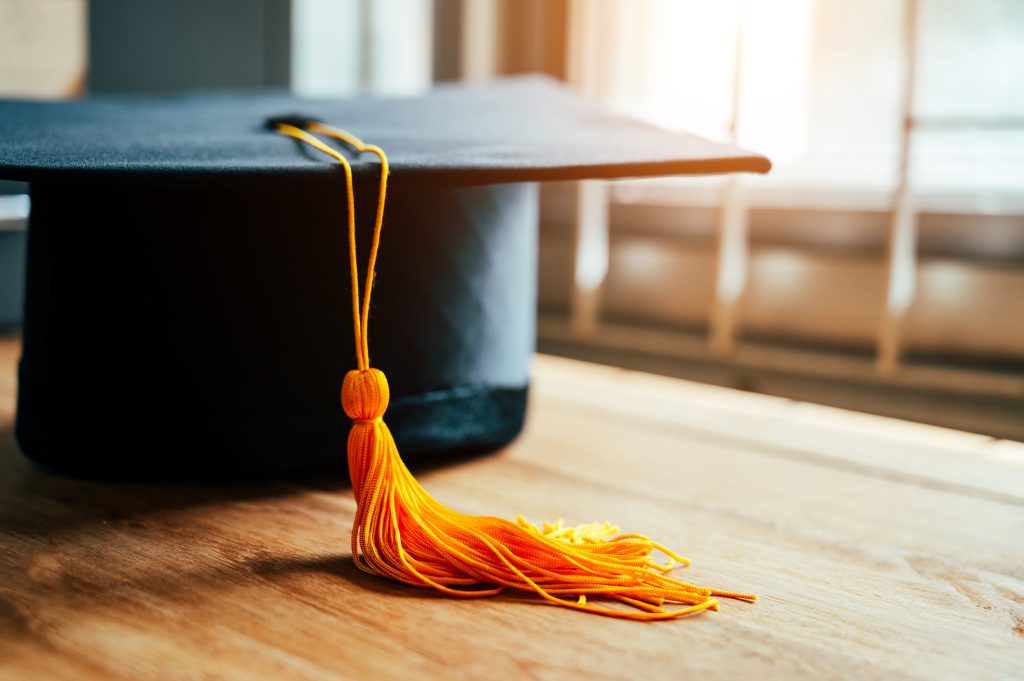 Black graduation cap and yellow tassel place on wooden table.