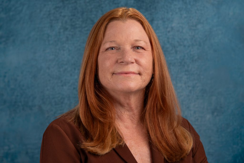 A portrait of Elizabeth O'Shea-West in front of a blue textures backdrop.